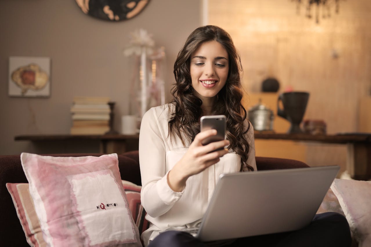 Woman Sitting on Sofa While Looking at Phone With Laptop 